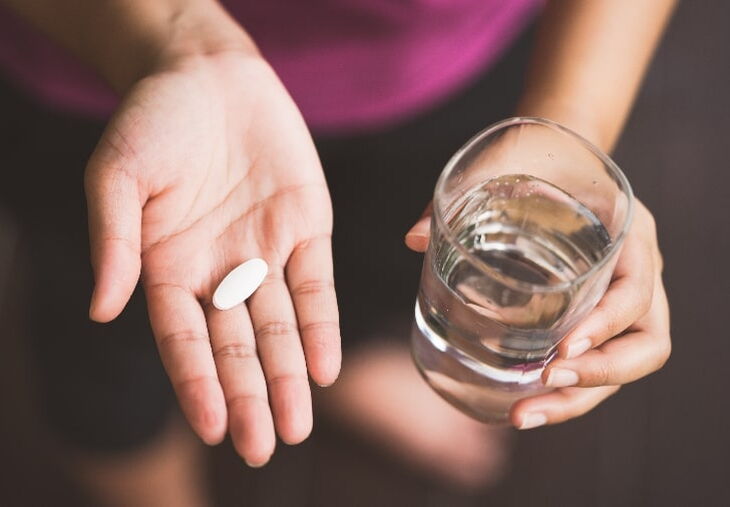 Person holding a pill in one hand and a glass of water in the other