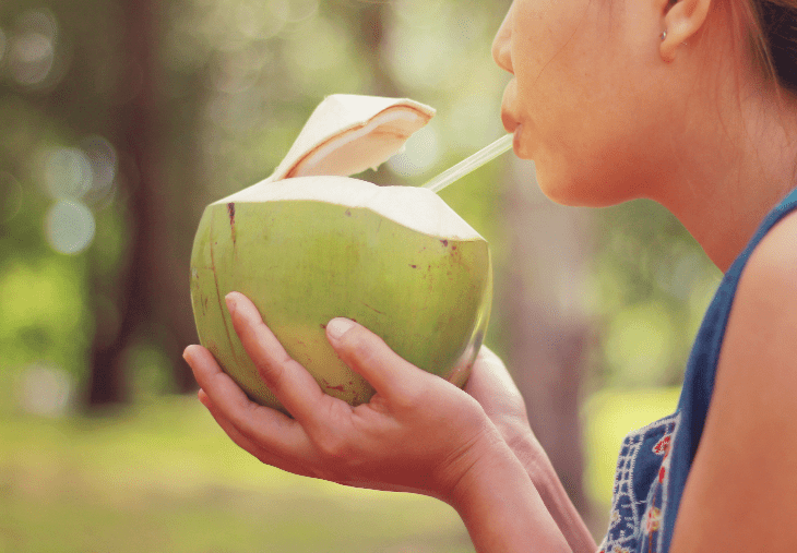 Woman drinking coconut water out of a whole coconut