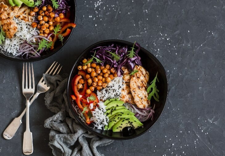 Chicken, rice, avocado, purple cabbage and red bell pepper in a bowl on a dark background