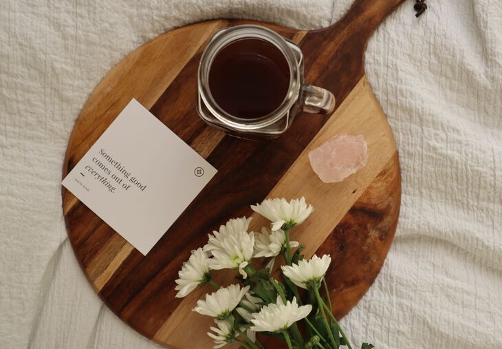 Affirmation card, black coffee, flowers and crystal on bed