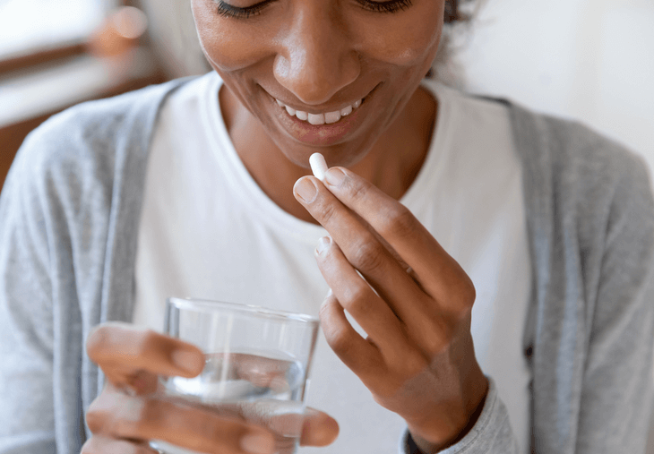 black woman with glass of water and supplement