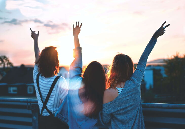 three women at sunset with arms in the air excited